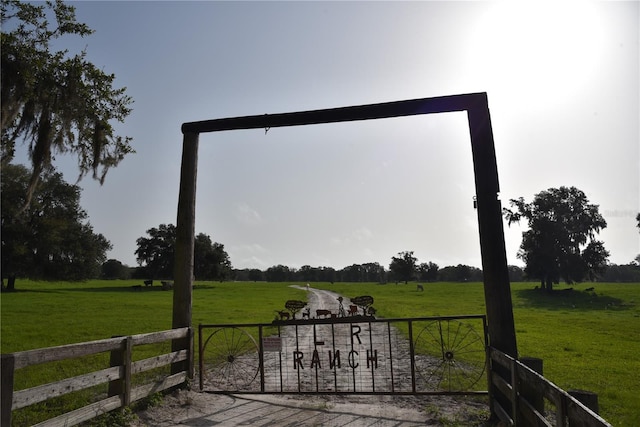 view of gate featuring a lawn, fence, and a rural view