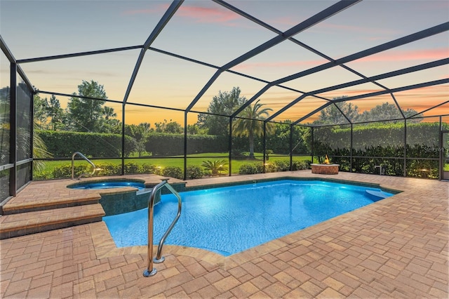 pool at dusk featuring a pool with connected hot tub, glass enclosure, and a patio area