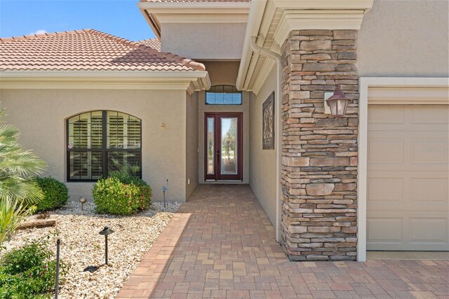 view of exterior entry featuring stucco siding, an attached garage, and stone siding