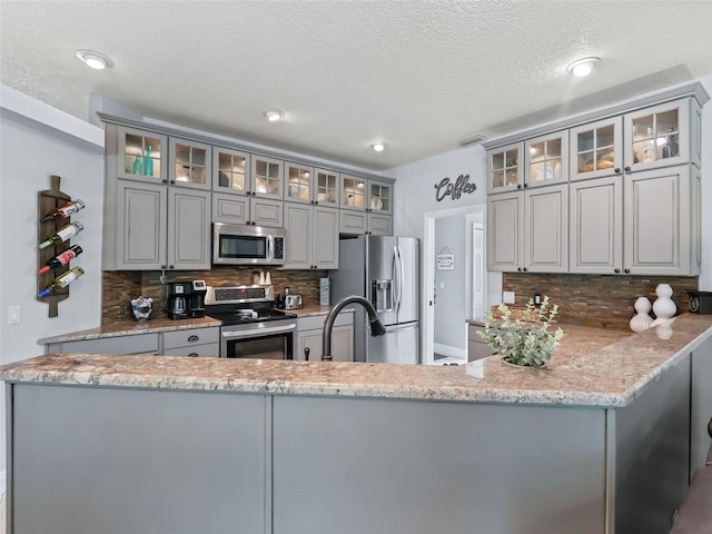 4658 W Hacienda Dr, Beverly Hills, FL 34465 - kitchen featuring a peninsula, a textured ceiling, decorative backsplash, gray cabinetry, and appliances with stainless steel finishes