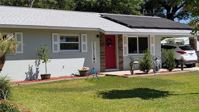 view of front of home with roof with shingles, a front lawn, an attached carport, stone siding, and roof mounted solar panels