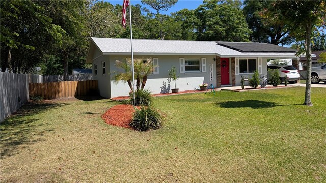 ranch-style house featuring concrete block siding, an attached carport, solar panels, fence, and a front yard