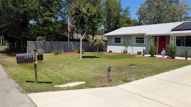 single story home with fence, a front yard, and solar panels