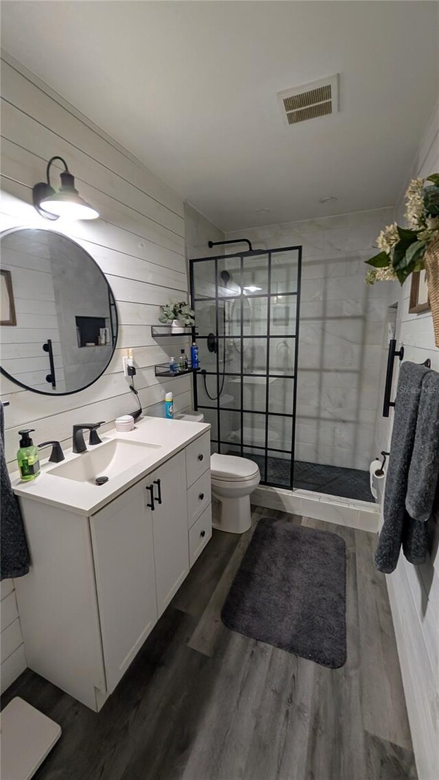 bathroom featuring a tile shower, wood finished floors, visible vents, and toilet