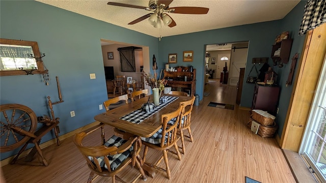 dining area with light wood-style flooring, a textured ceiling, a ceiling fan, and baseboards