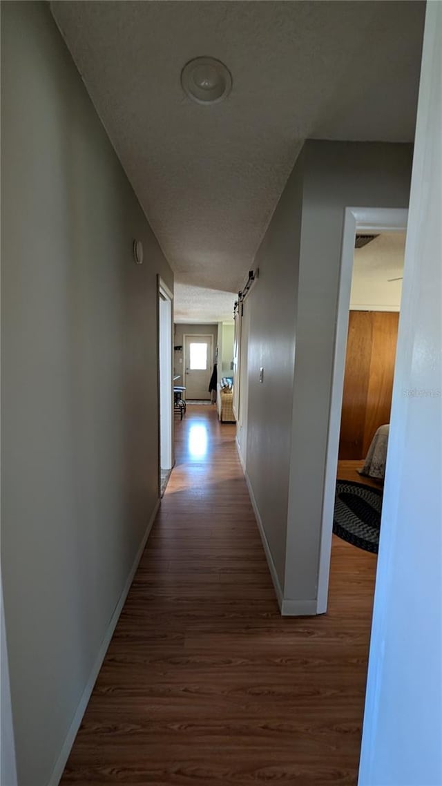 corridor featuring baseboards, visible vents, dark wood-type flooring, and a textured ceiling