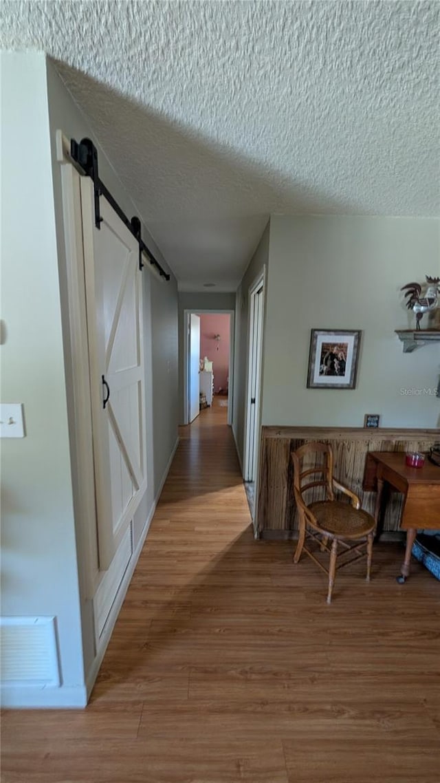 corridor featuring a barn door, a textured ceiling, visible vents, and light wood-type flooring