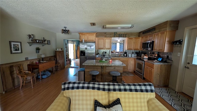 kitchen featuring backsplash, appliances with stainless steel finishes, a center island, and wood finished floors