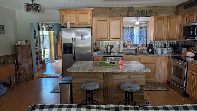 kitchen featuring light stone counters, wood finished floors, a sink, stainless steel appliances, and backsplash