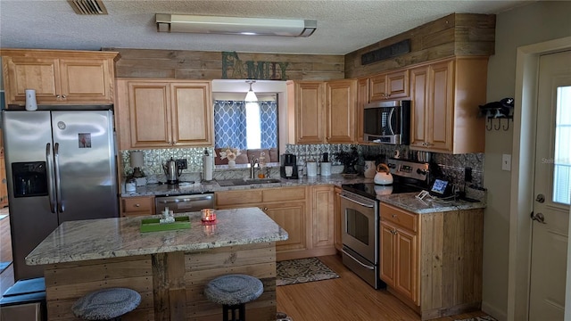 kitchen featuring tasteful backsplash, a sink, light wood-style floors, appliances with stainless steel finishes, and light stone countertops