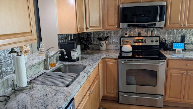 kitchen with backsplash, appliances with stainless steel finishes, light stone counters, and a sink