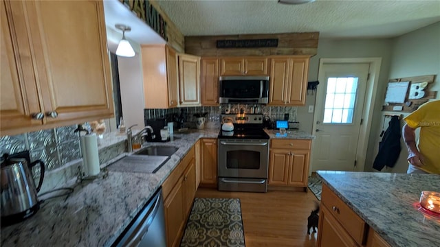 kitchen featuring light stone counters, a sink, light wood-style floors, tasteful backsplash, and appliances with stainless steel finishes