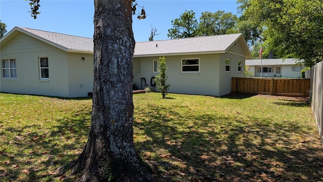 rear view of house featuring a lawn, a shingled roof, and fence