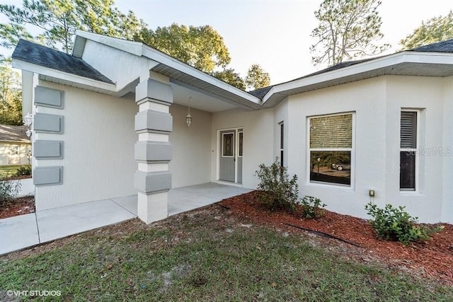 view of exterior entry featuring stucco siding and a patio