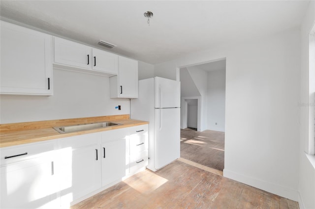 kitchen featuring a sink, light wood-style flooring, white cabinets, visible vents, and freestanding refrigerator