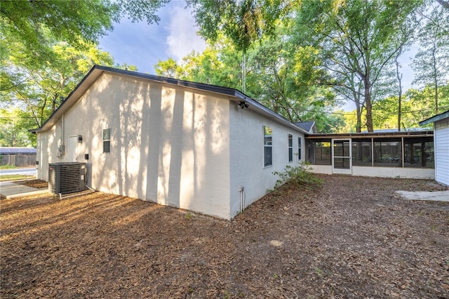 view of home's exterior with stucco siding, a sunroom, and central AC