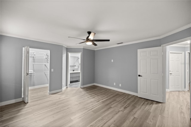 unfurnished bedroom featuring a spacious closet, visible vents, light wood-type flooring, crown molding, and baseboards