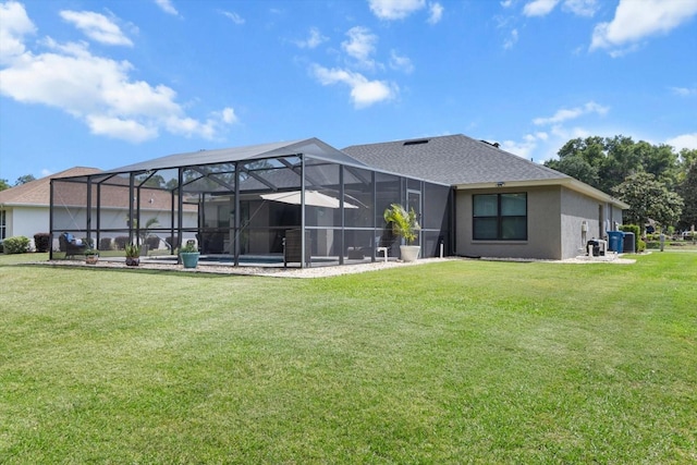 rear view of property featuring a shingled roof, glass enclosure, central AC, stucco siding, and a lawn
