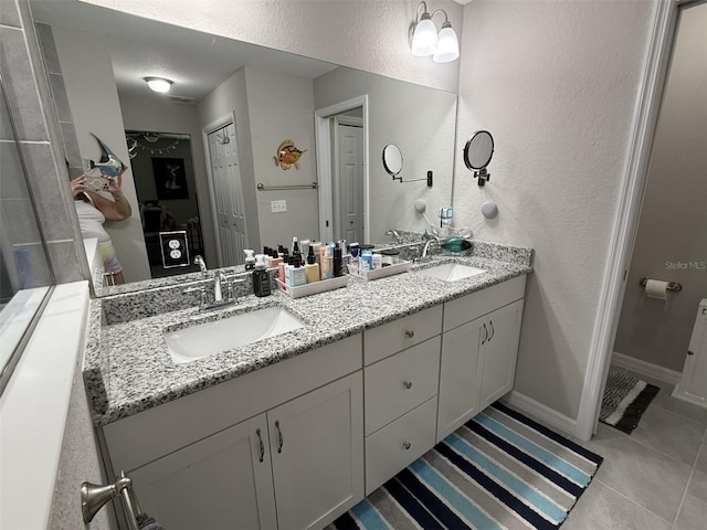 full bath featuring double vanity, a textured wall, tile patterned flooring, and a sink