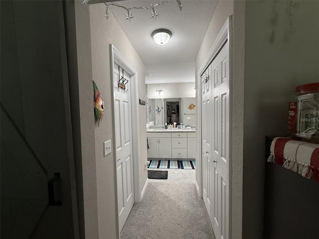 corridor with light colored carpet, a textured ceiling, and a textured wall