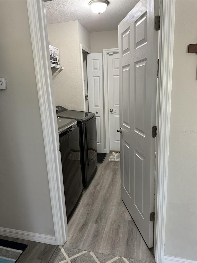 washroom with laundry area, a textured ceiling, separate washer and dryer, and light wood finished floors
