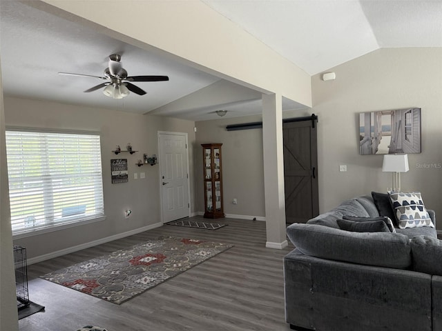 living room with wood finished floors, a ceiling fan, baseboards, a barn door, and vaulted ceiling
