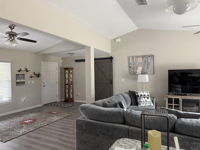 living area featuring wood finished floors, a ceiling fan, baseboards, a barn door, and lofted ceiling
