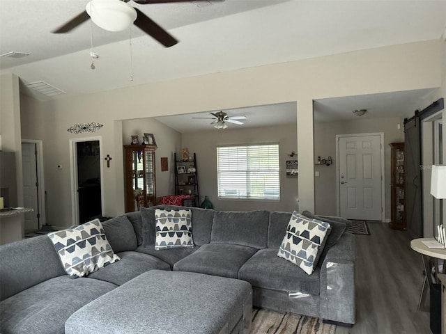 living room with a barn door, visible vents, wood finished floors, and a ceiling fan