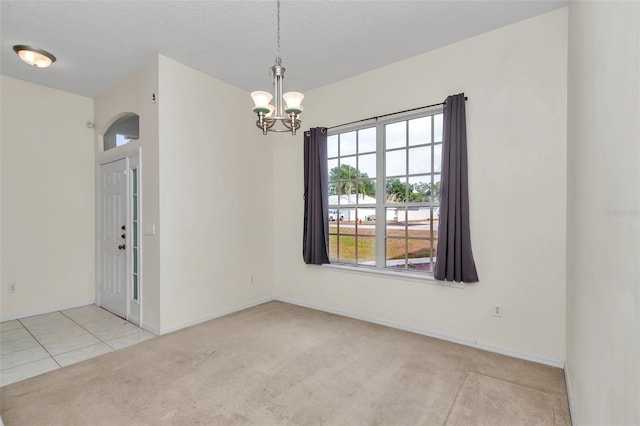 empty room featuring a chandelier, carpet floors, baseboards, and tile patterned flooring