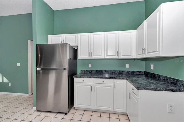 kitchen with freestanding refrigerator, dark countertops, white cabinets, light tile patterned floors, and a textured ceiling