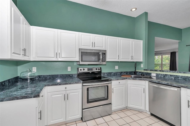 kitchen with stainless steel appliances, a sink, dark countertops, white cabinetry, and a textured ceiling