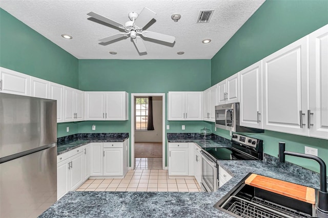 kitchen with appliances with stainless steel finishes, a sink, a textured ceiling, white cabinets, and light tile patterned flooring