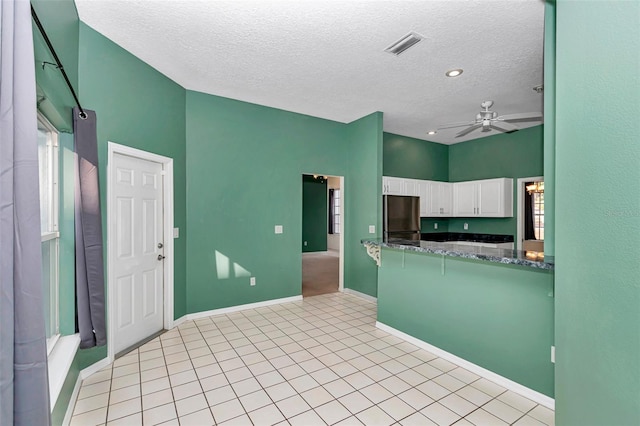 kitchen with freestanding refrigerator, a textured ceiling, white cabinets, a ceiling fan, and dark stone countertops