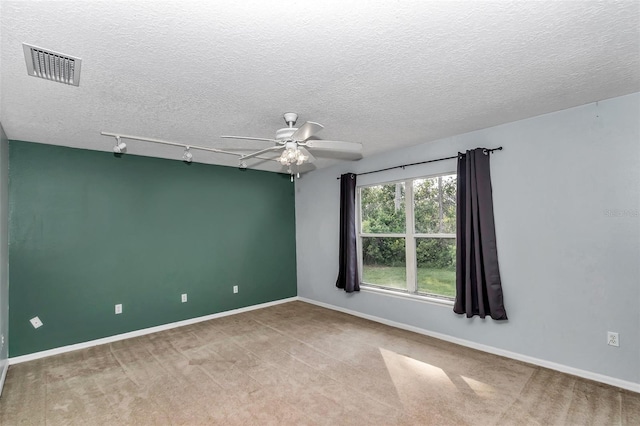 carpeted spare room featuring a ceiling fan, track lighting, a textured ceiling, and baseboards
