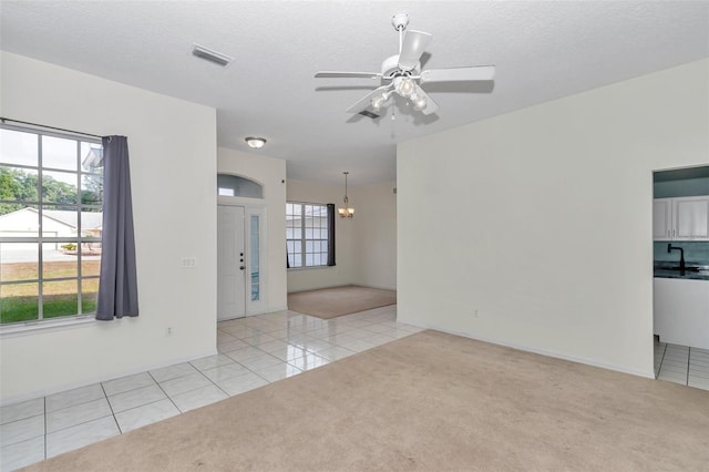 spare room with light colored carpet, light tile patterned flooring, a chandelier, ceiling fan, and a textured ceiling