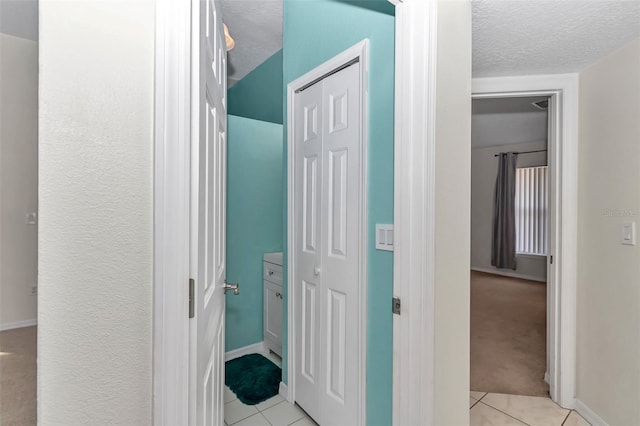 hall with light tile patterned flooring, a textured ceiling, baseboards, and light colored carpet