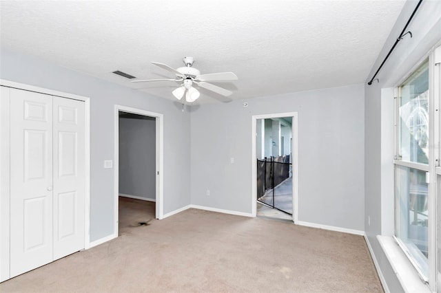 unfurnished bedroom with light colored carpet, a closet, a textured ceiling, baseboards, and a ceiling fan