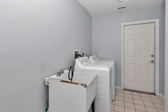 clothes washing area with independent washer and dryer, light tile patterned floors, a textured ceiling, and baseboards