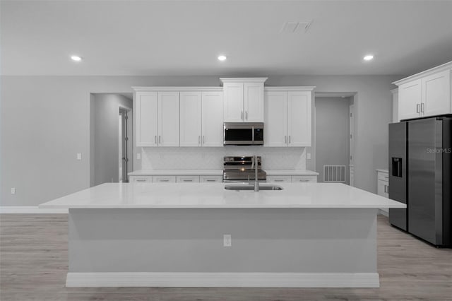 kitchen with visible vents, tasteful backsplash, a center island with sink, stainless steel appliances, and white cabinetry