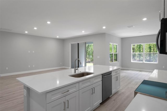 kitchen featuring open floor plan, a center island with sink, a sink, light wood finished floors, and dishwasher
