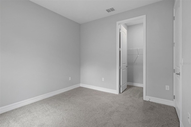 unfurnished bedroom with a walk in closet, carpet floors, baseboards, visible vents, and a closet