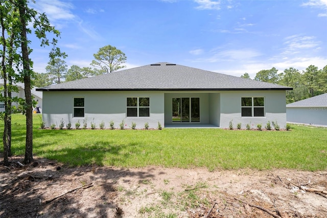 rear view of house with a yard, a shingled roof, and stucco siding
