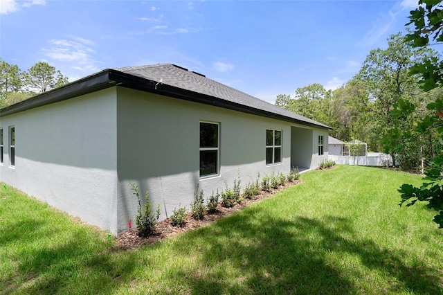 view of side of home featuring a shingled roof, stucco siding, a yard, and fence