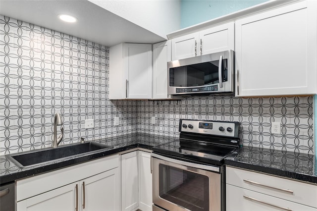 kitchen featuring dark countertops, a sink, stainless steel appliances, white cabinets, and backsplash