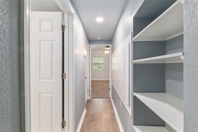 corridor featuring a textured wall, baseboards, and wood finished floors