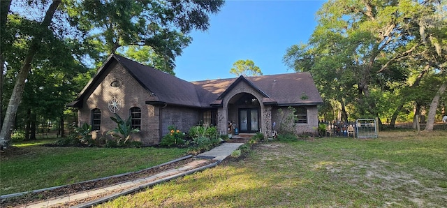 tudor-style house with a front lawn, a shingled roof, french doors, and brick siding