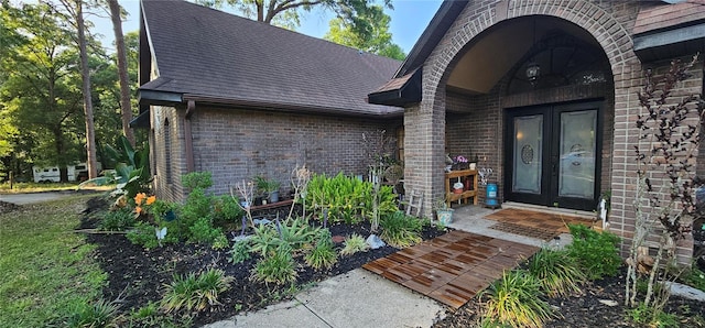 property entrance featuring roof with shingles, french doors, and brick siding