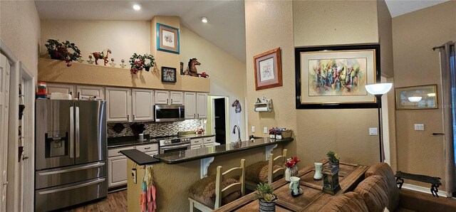 kitchen featuring a breakfast bar area, appliances with stainless steel finishes, dark countertops, dark wood-style floors, and vaulted ceiling
