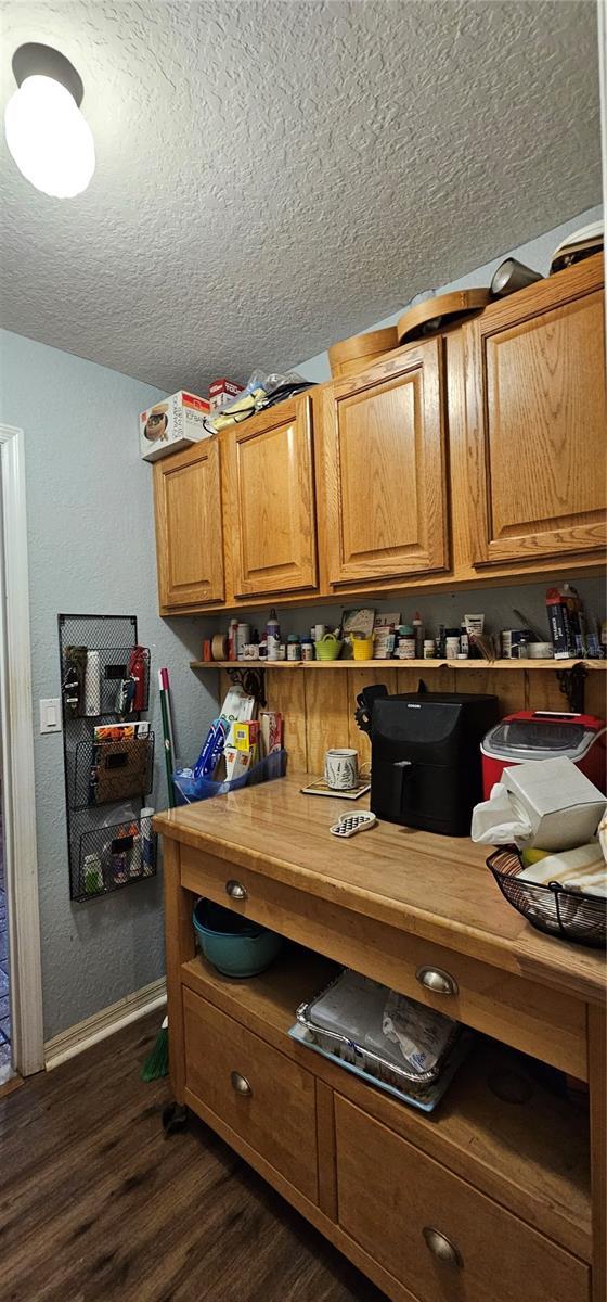 kitchen featuring baseboards, a textured ceiling, dark wood finished floors, and brown cabinets