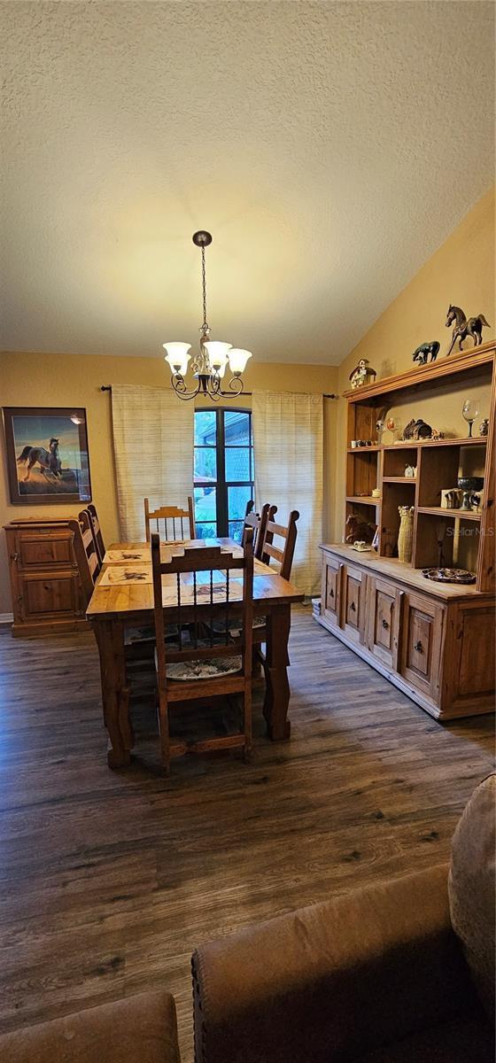 dining area featuring an inviting chandelier, a textured ceiling, lofted ceiling, and dark wood-type flooring